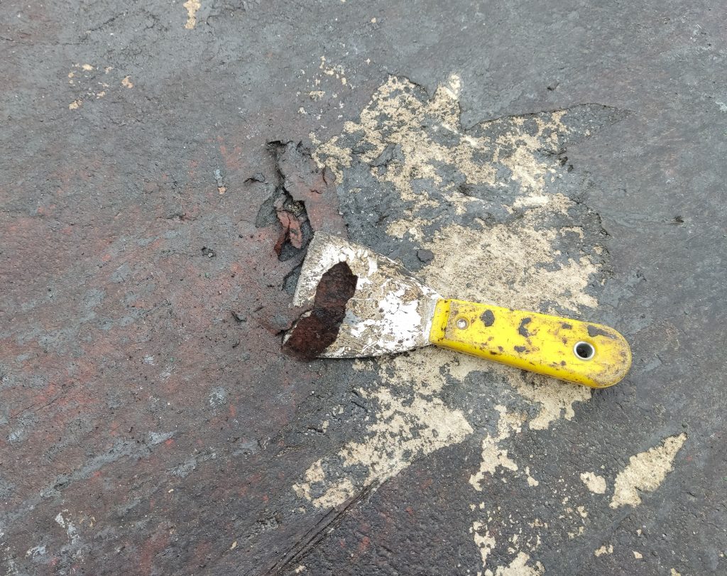 Espátula metálica raspando asfalto mal adherido