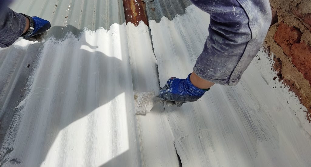 Aplicación de impermeabilizante con brocha sobre un techo de tejas de zinc